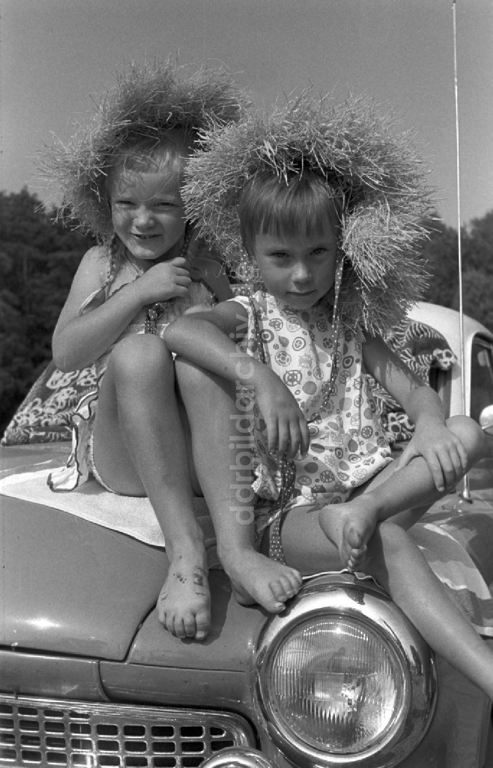 DDR-Fotoarchiv: Neuruppin OT Stendenitz - Zwei Mädchen mit Strohhüten sitzen barfuß auf einer Motorhaube eines Wartburg 311 in Brandenburg
