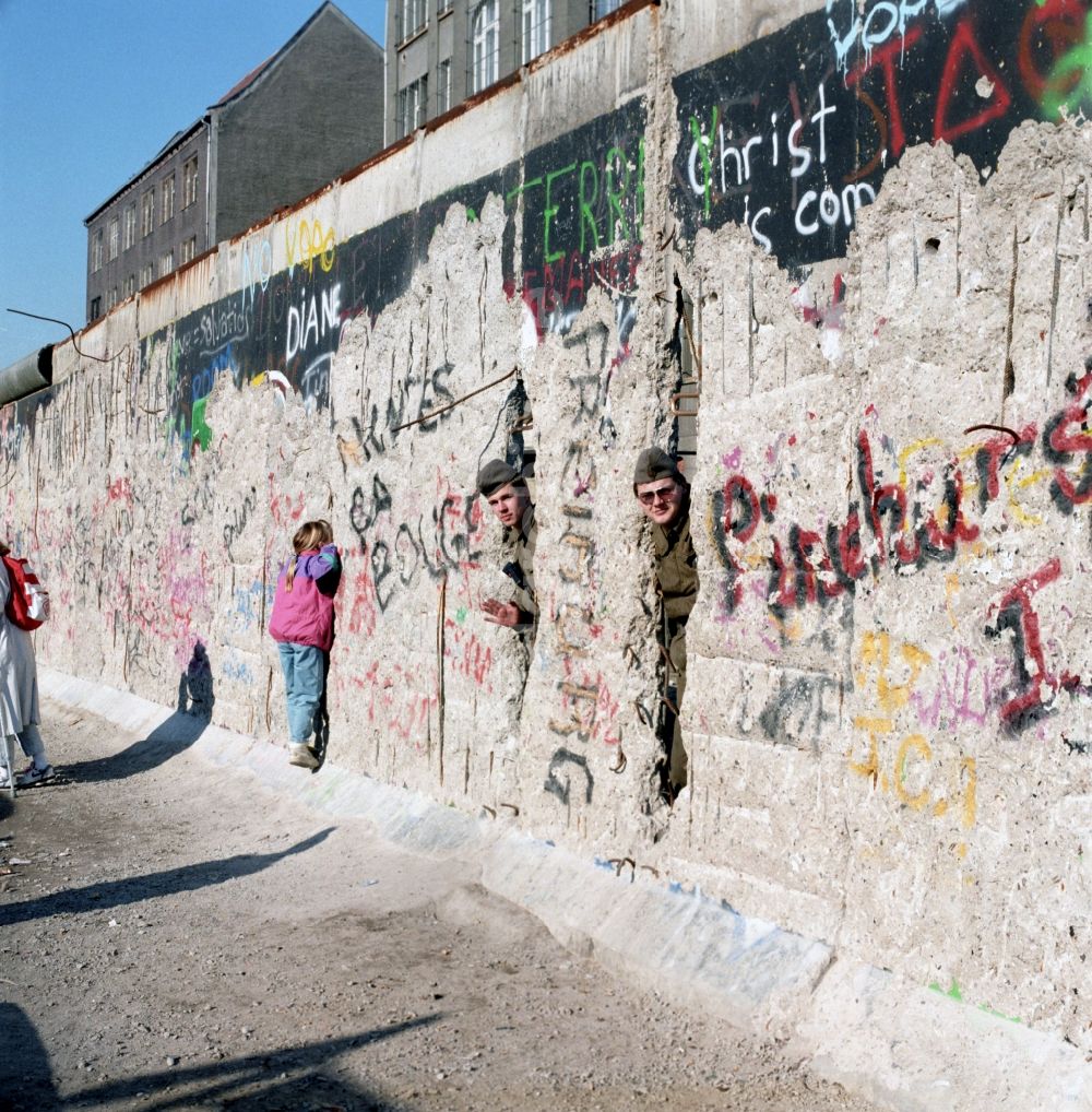 DDR-Bildarchiv: Berlin - Zwei Soldaten der Grenztruppen der DDR schauen durch ein Loch in der Berliner Mauer in Berlin