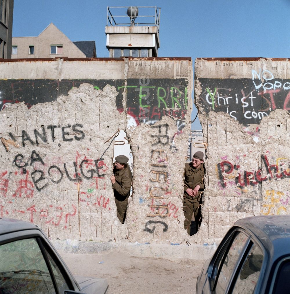 Berlin: Zwei Soldaten der Grenztruppen der DDR schauen durch ein Loch in der Berliner Mauer in Berlin